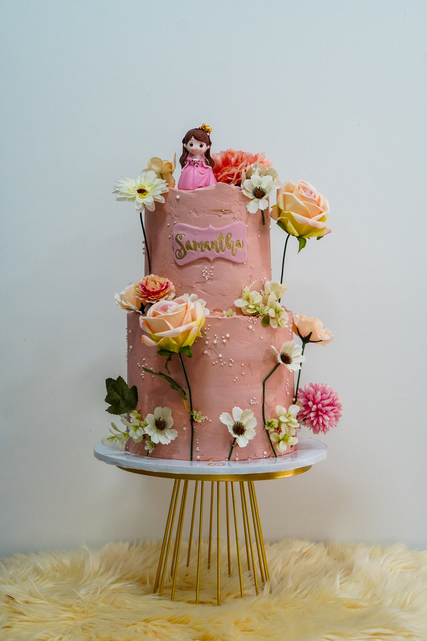 Pink two-tier floral birthday cake with princess topper and assorted flowers