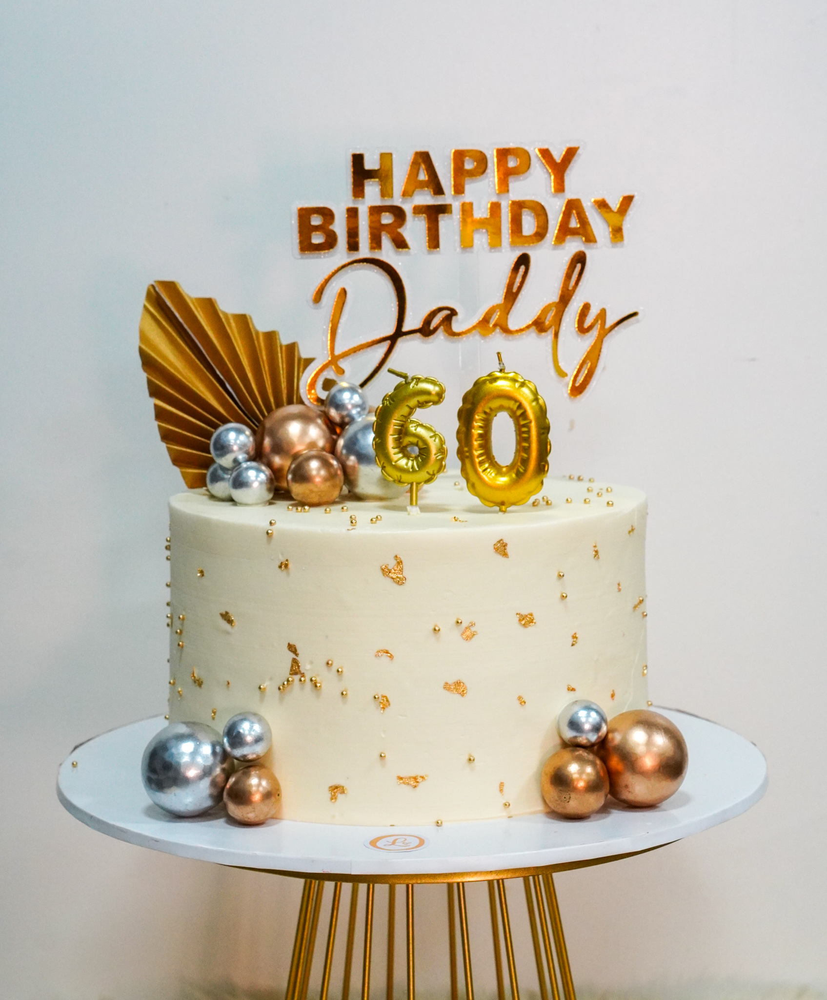 Elegant white birthday cake with gold and silver metallic spheres, gold flakes, and a 'Happy Birthday Daddy 60' topper