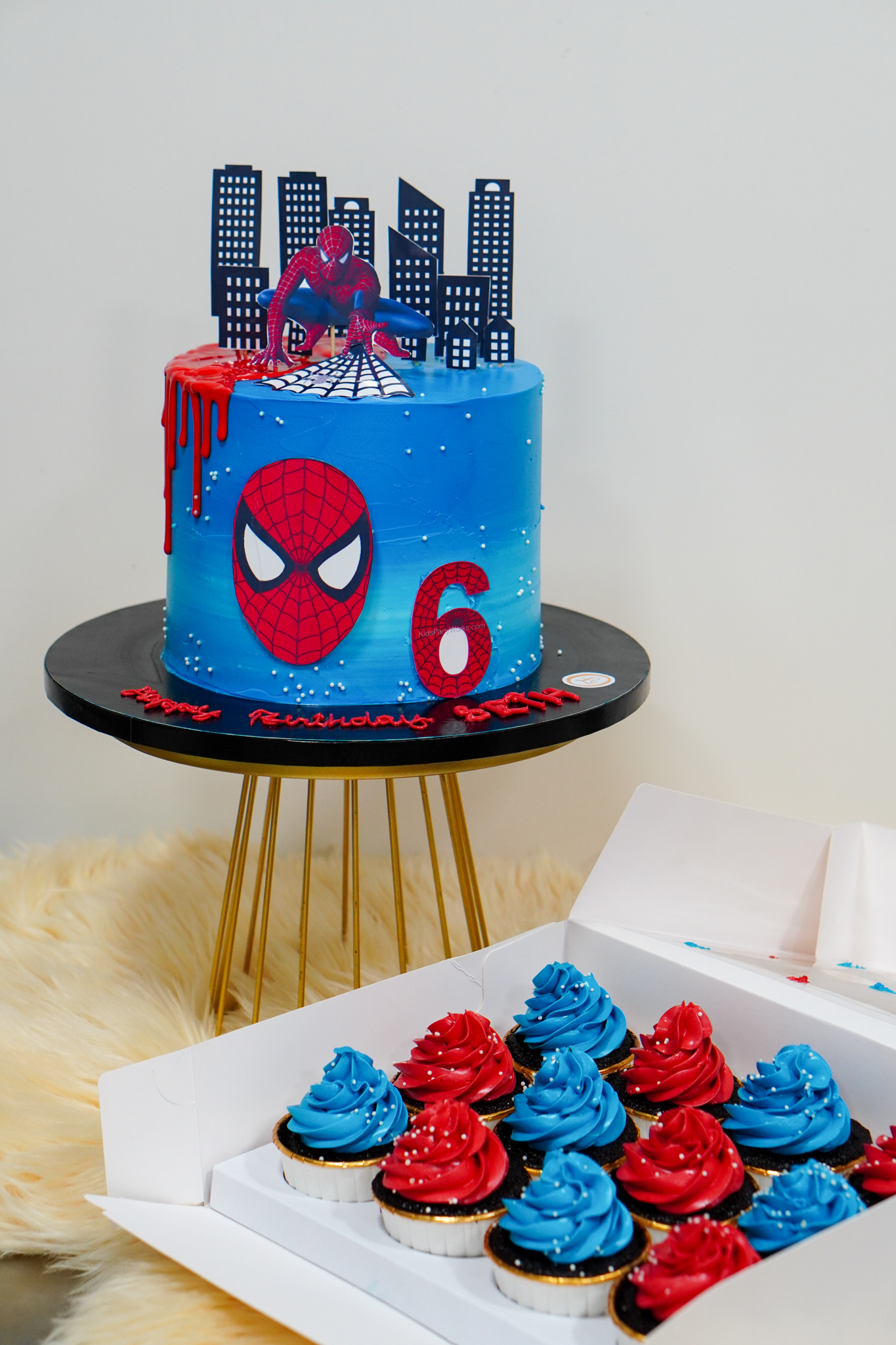 Spider-Man themed 6th birthday cake in blue ombré with city skyline toppers, web design, Spider-Man figurine, and matching red and blue cupcakes