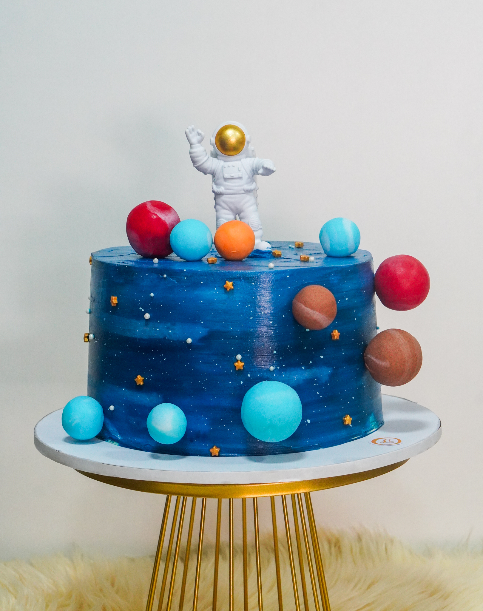 Blue buttercream birthday cake with a space theme, featuring an astronaut topper, colorful planets, and star accents