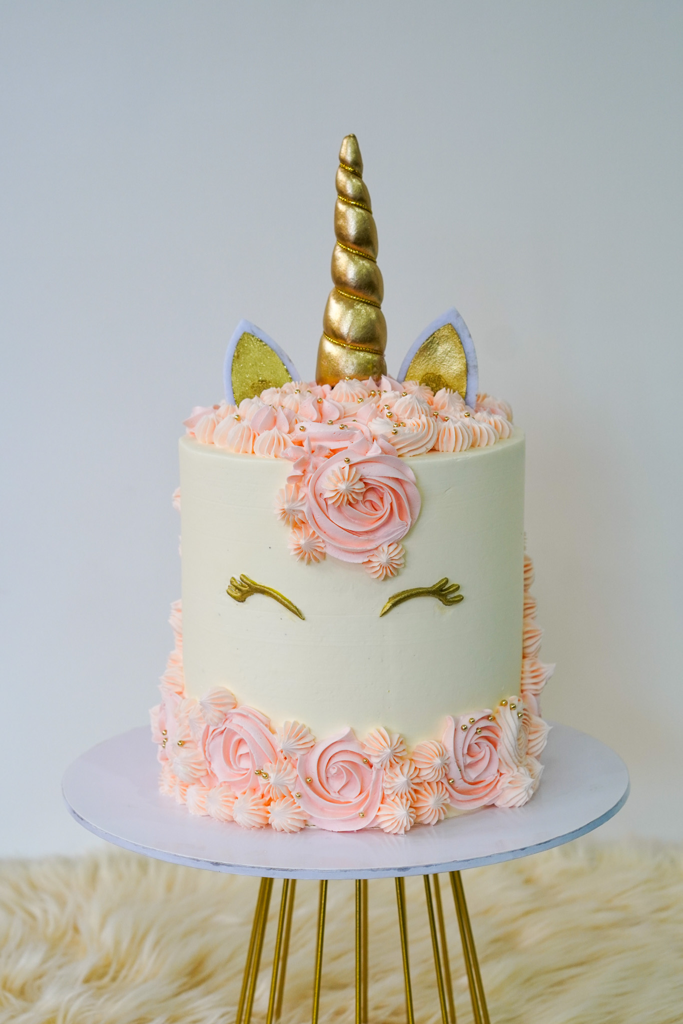 Unicorn themed buttercream cake with gold horn, gold ears, pink rosette mane, and closed eye design